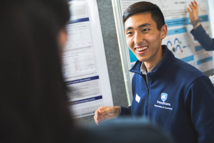 Kueyoung Kim stands smiling in front of his poster wearing a navy blue Penn State Department of Chemistry pullover.